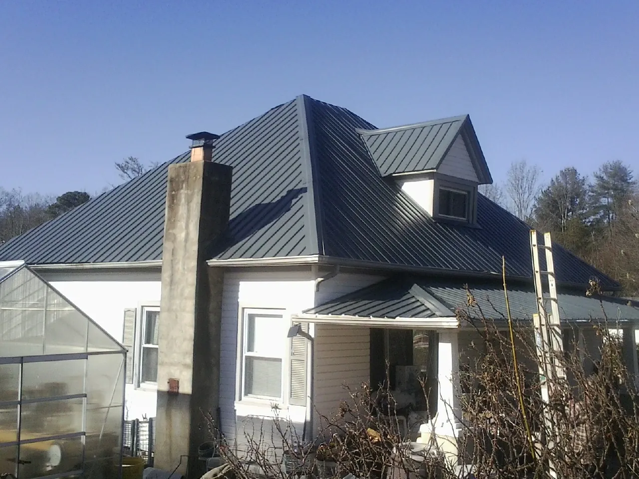 Dark blue standing seam metal roof on a white farmhouse with dormer — Slate & Tile Roof Repair by Roofing Brothers in What Cheer