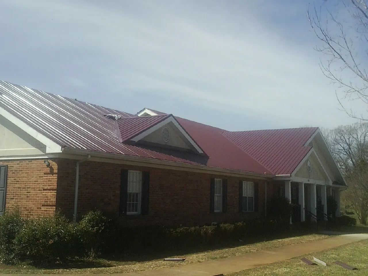 Red metal roof with gabled entries on a long brick building, from a Hail Damage Roof Repair job in What Cheer
