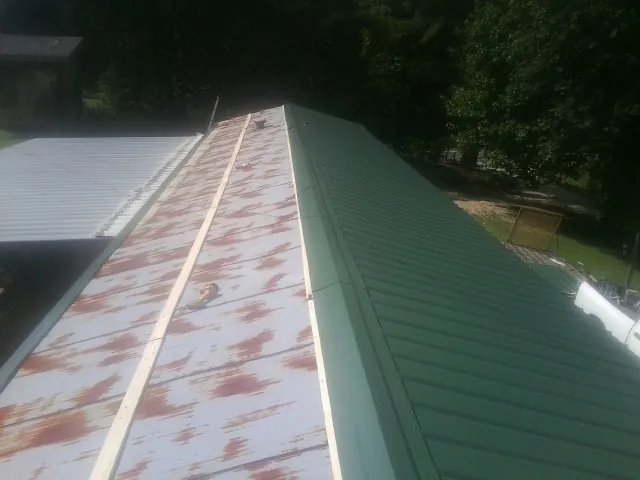 Old rusted panels beside newly installed green metal roofing — Wind Damage Roof Repair by Roofing Brothers in What Cheer