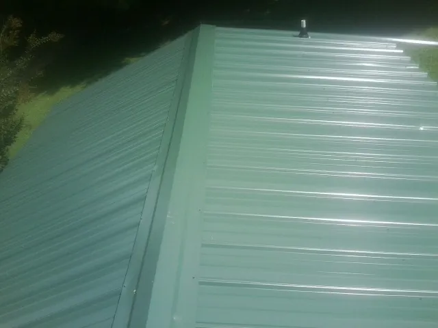 New green metal panels meeting at the ridge of a roof — Flat Roof Repair work by our crew in What Cheer