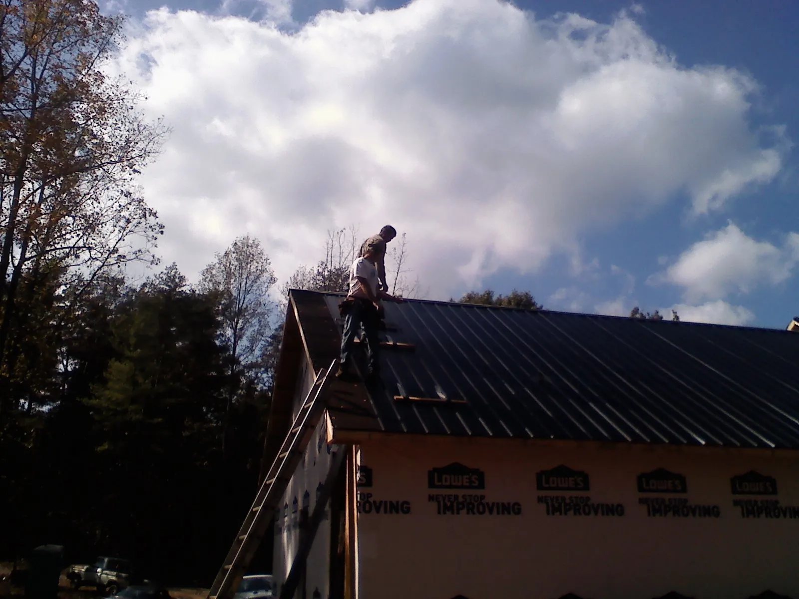 Roofer fastening dark metal panels high against a cloudy sky, from a Roof Inspection job in What Cheer