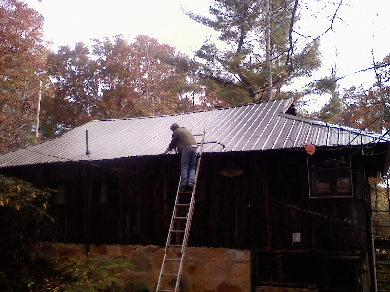 Roofer on a ladder working along the edge of a cabin metal roof in What Cheer