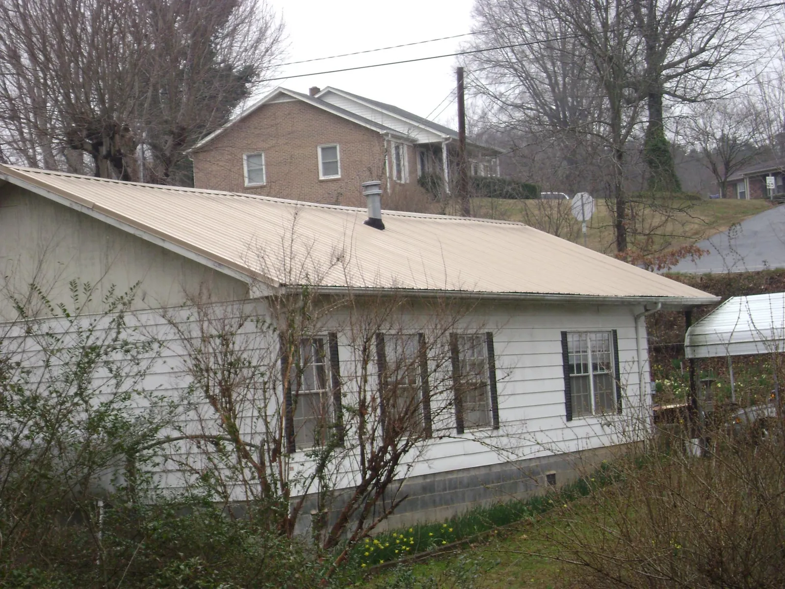 Tan metal roof on a white sided house set into a hillside — Commercial Roofing by Roofing Brothers in What Cheer