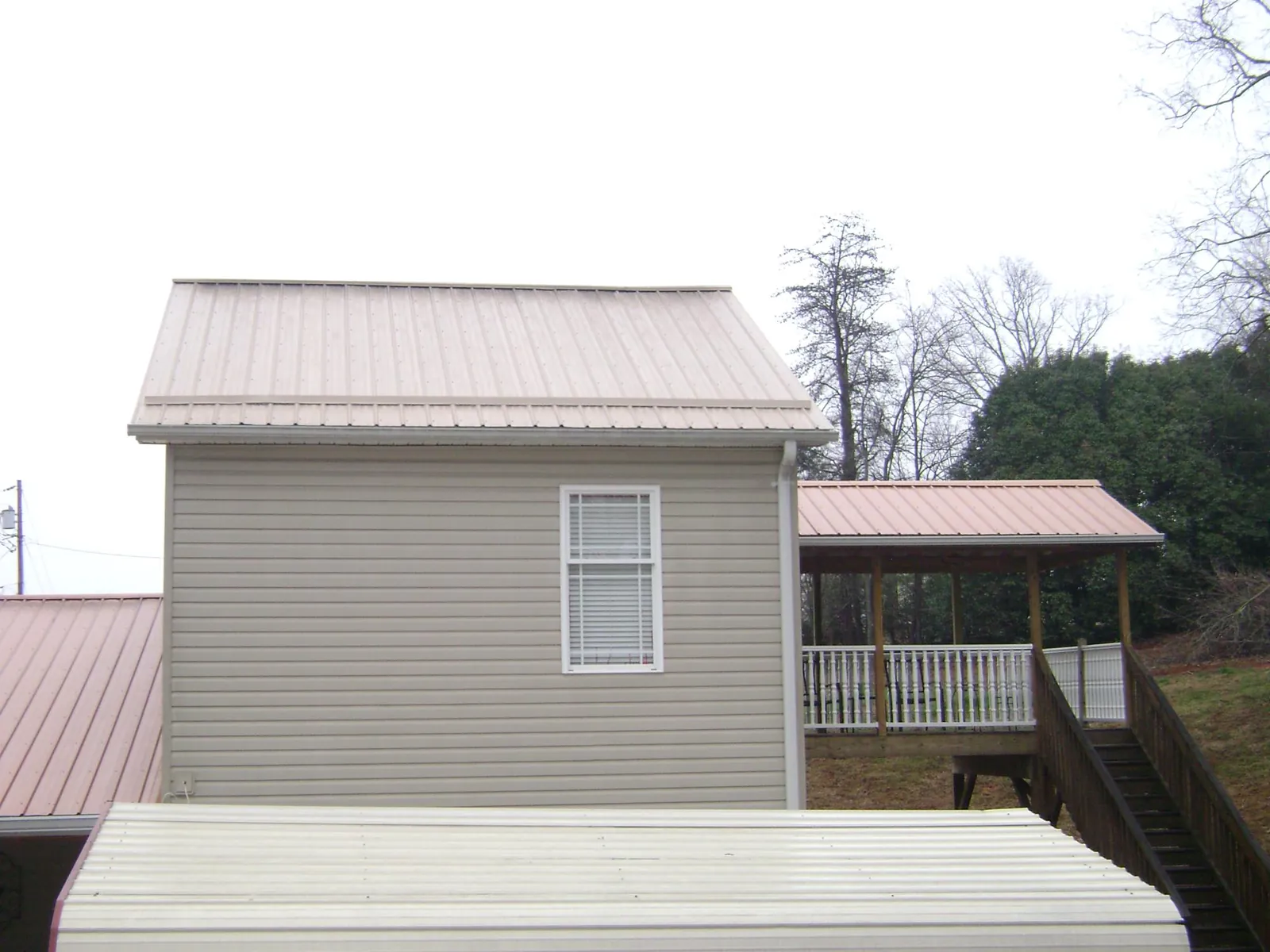 Tan metal roofs on a two story addition and attached porch, from a Roof Replacement job in What Cheer